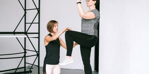 An elderly woman performs exercises with a fitness coach, focusing on a healthy lifestyle and wellness indoors.